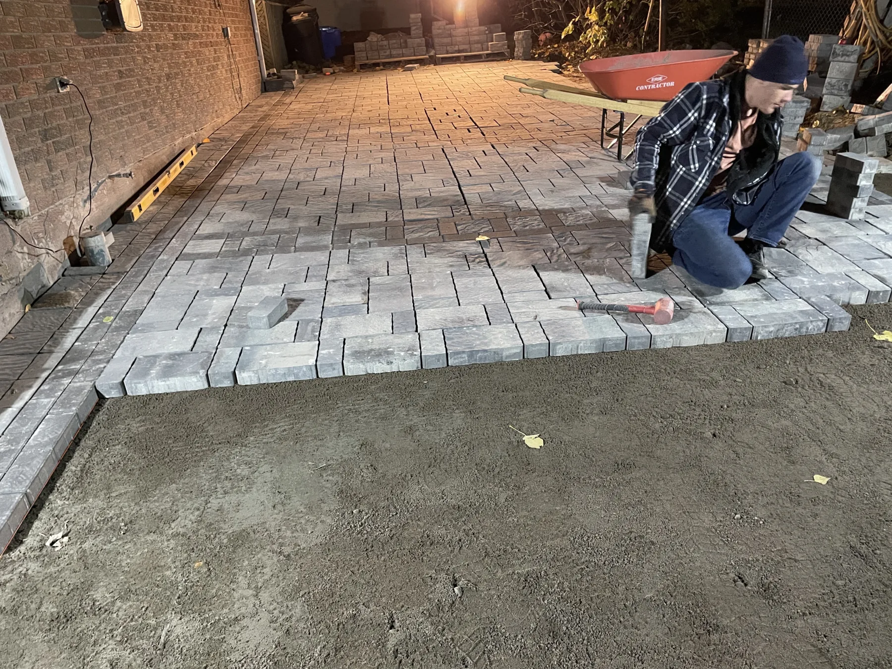 Bouwers Design Landscaping crew member hand-laying an interlock paver patio against a home in North Bay, Ontario, with the paver pattern and edge transition visible.