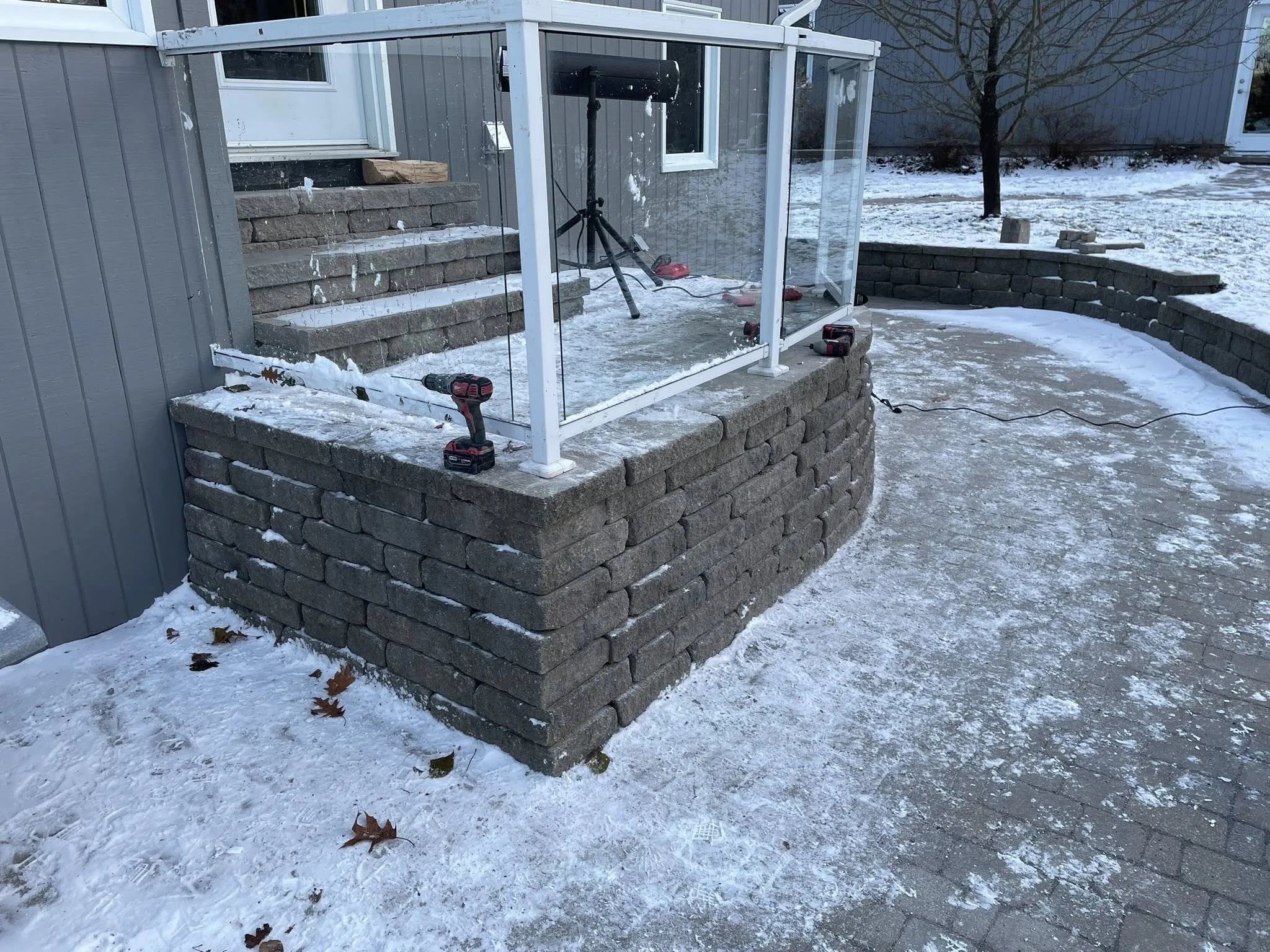 Segmental block retaining wall and integrated stairs built by Bouwers Design Landscaping on a residential property in North Bay, Ontario, set against a glass-railing entry.